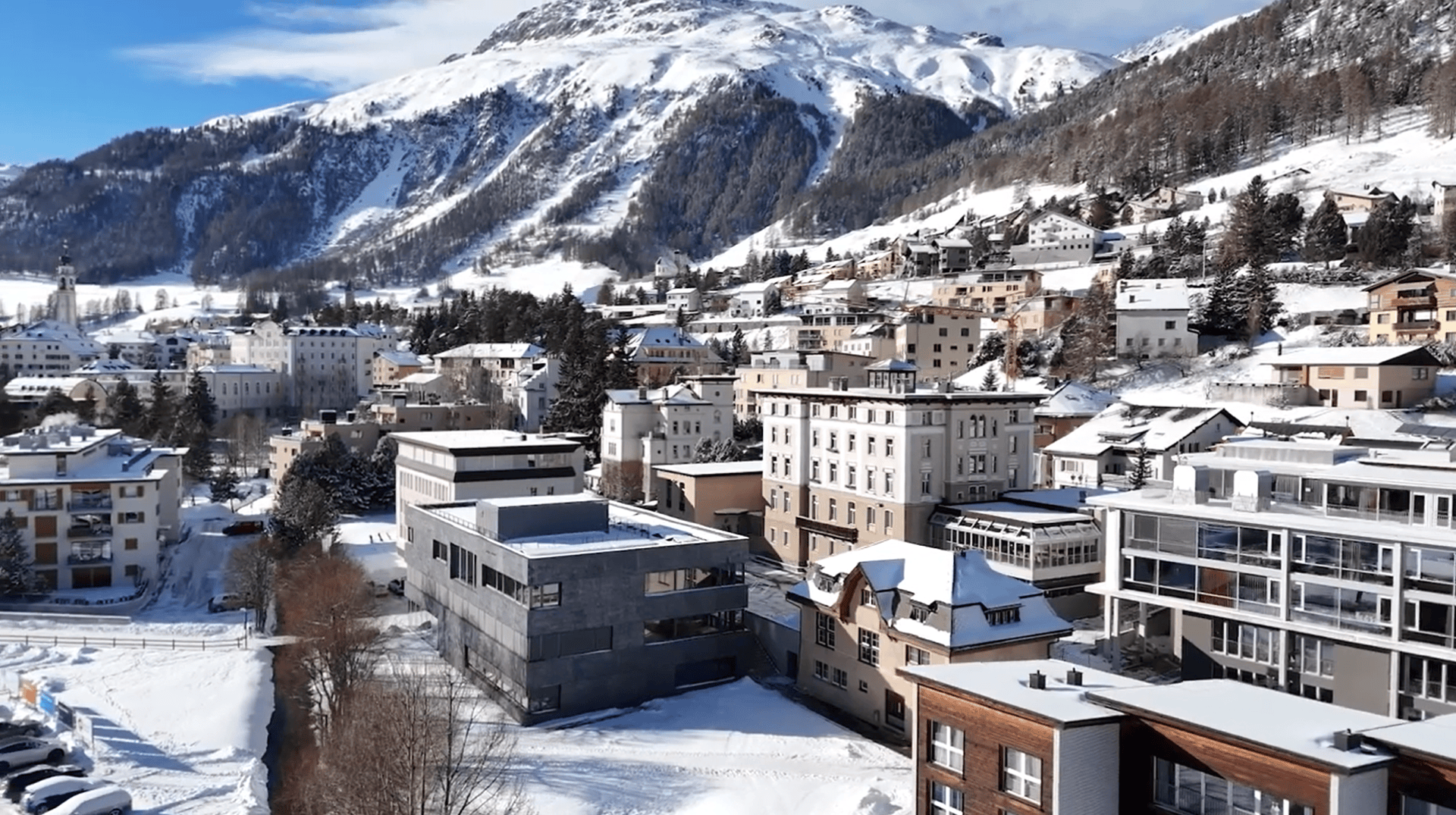 Die schneebedeckten Gebäude in Samedan heben sich vor dem Hintergrund hoher, schneebedeckter Berge unter einem strahlend blauen Himmel ab und bilden so eine malerische Winterlandschaft.