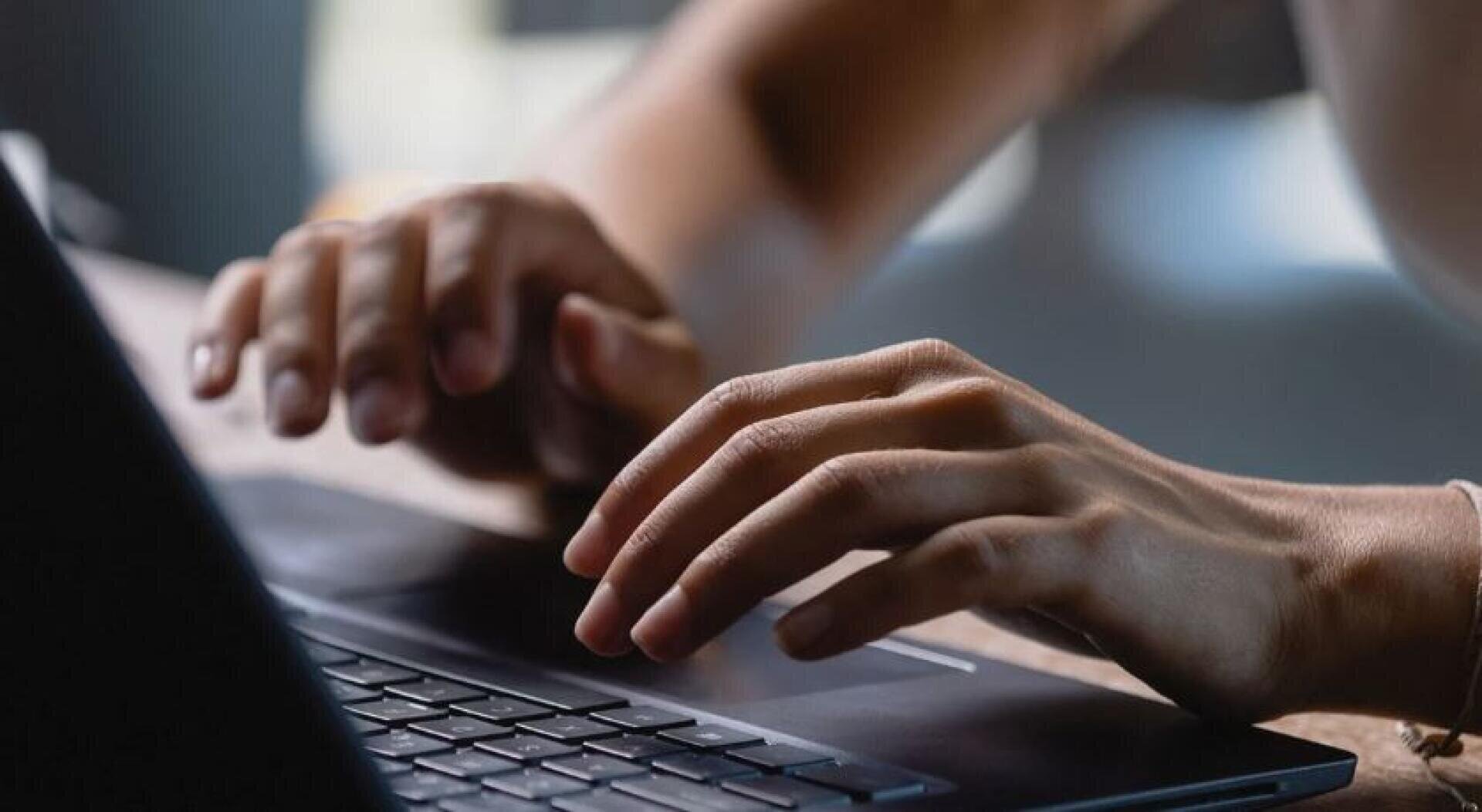 Nahaufnahme einer Person, die mit den Händen auf einer Laptoptastatur tippt, mit einem unscharfen Hintergrund, der eine Innenraumumgebung suggeriert.
