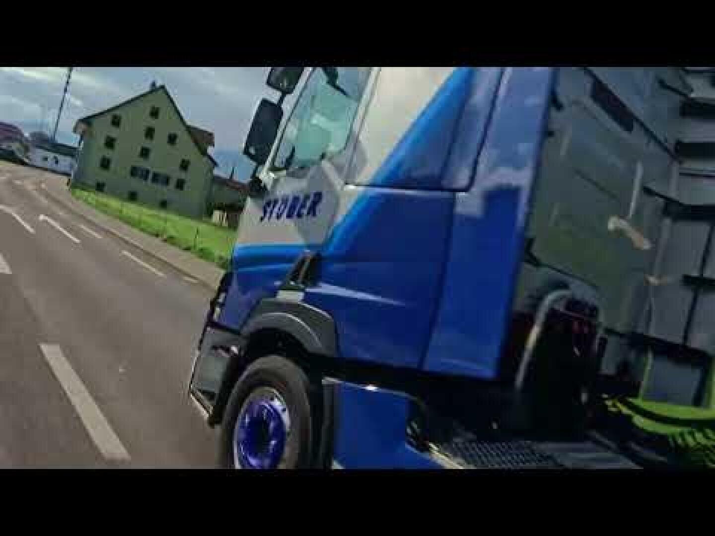 Ein blauer Lkw mit der Aufschrift „STOER“ fährt eine Landstraße entlang, im Hintergrund sind unter einem teilweise bewölkten Himmel Gewächshäuser und Gras zu sehen.