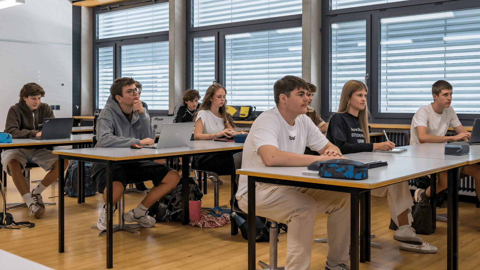 Eine Gruppe von Schülern, die an ihren Schreibtischen in einem Klassenzimmer sitzen und nach vorne blicken.