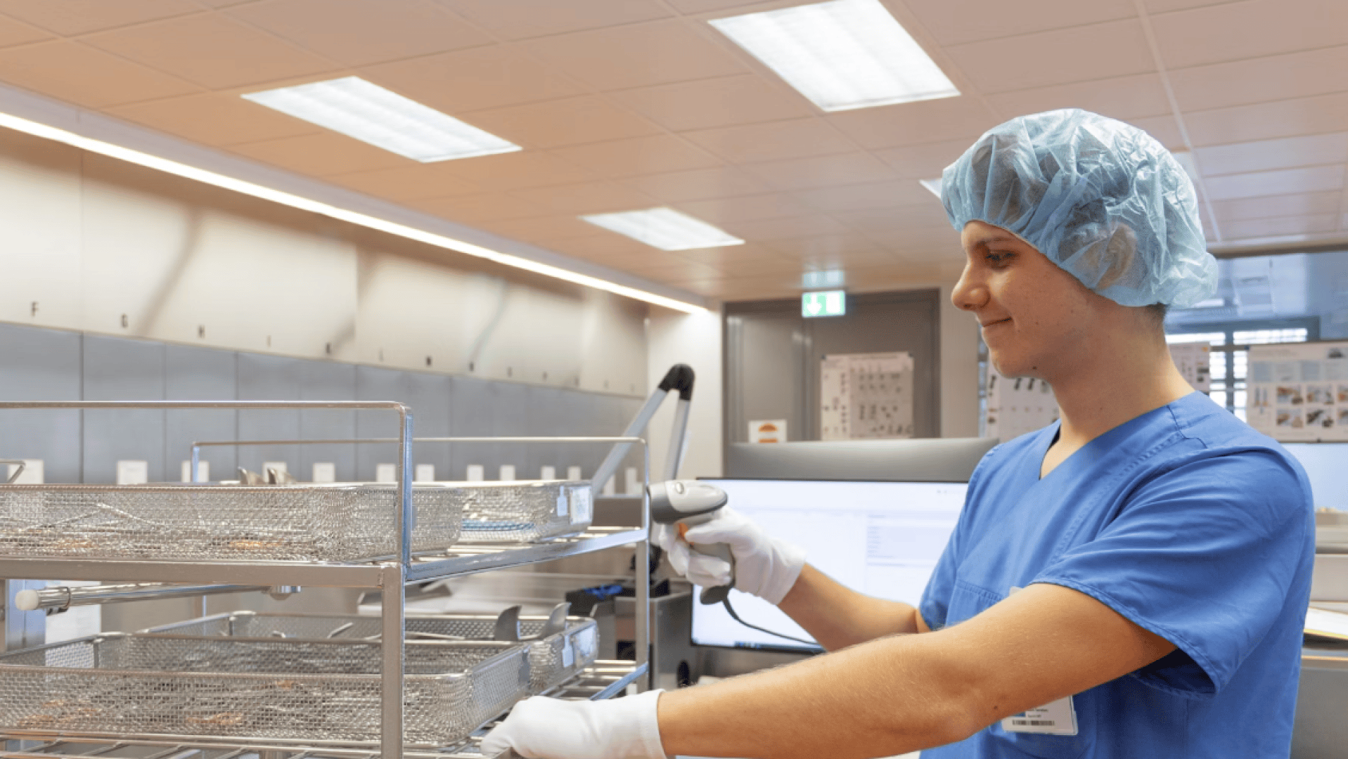 Ein Mitarbeiter des Gesundheitswesens in blauem Kittel, Haarnetz und Handschuhen benutzt einen Barcode-Scanner auf einem Metalltablett in einer sterilen, gut beleuchteten medizinischen Einrichtung.