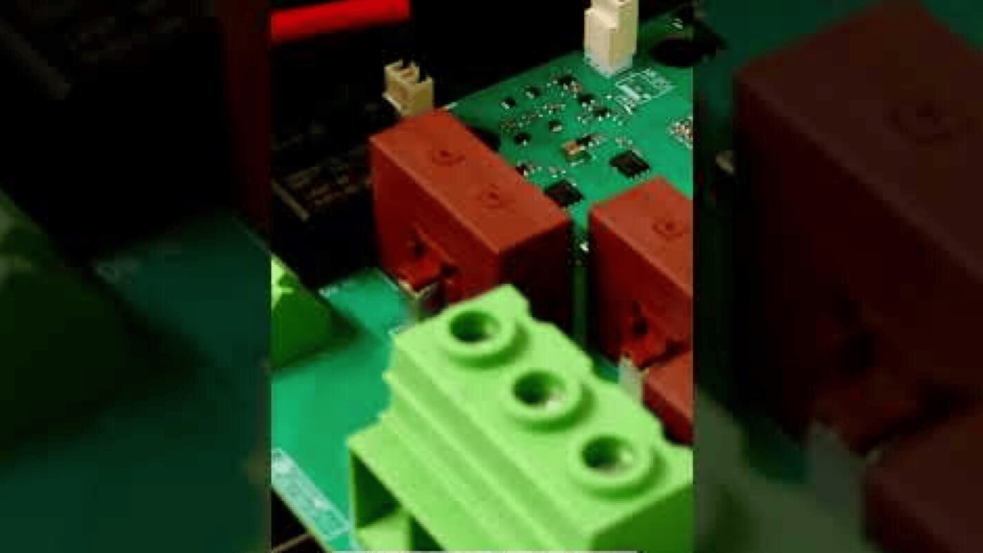 Nahaufnahme einer elektronischen Leiterplatte mit grünen und roten Anschlussklemmen und verschiedenen elektronischen Bauteilen.