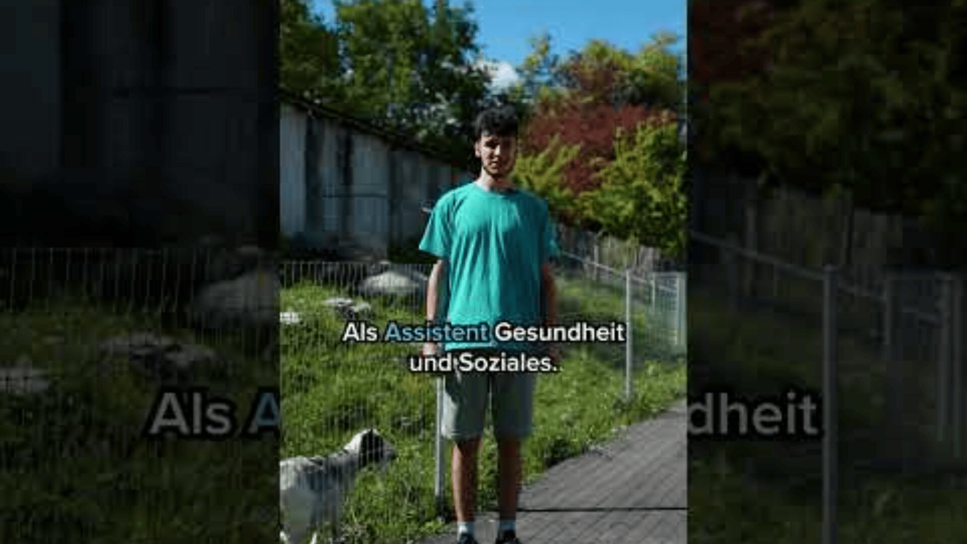 Ein junger Mann in einem blaugrünen Hemd steht auf einem Weg in der Nähe eines Drahtzauns und grüner Bäume, mit einem kleinen weißen Hund in der Nähe. Der deutsche Text auf dem Bild lautet: Als Assistent Gesundheit und Soziales.
