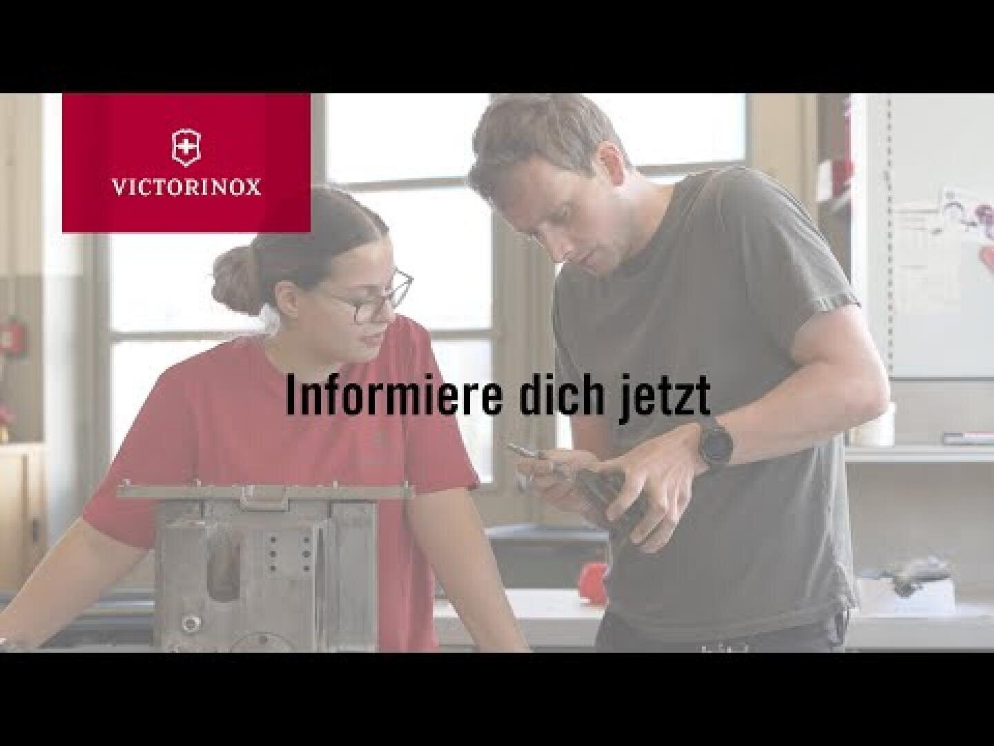 Ein Mann und eine Frau untersuchen gemeinsam einen Metallgegenstand in einer Werkstatt. Das Victorinox-Logo erscheint oben links. Der deutsche Text in der Mitte lautet: "Informiere dich jetzt".
