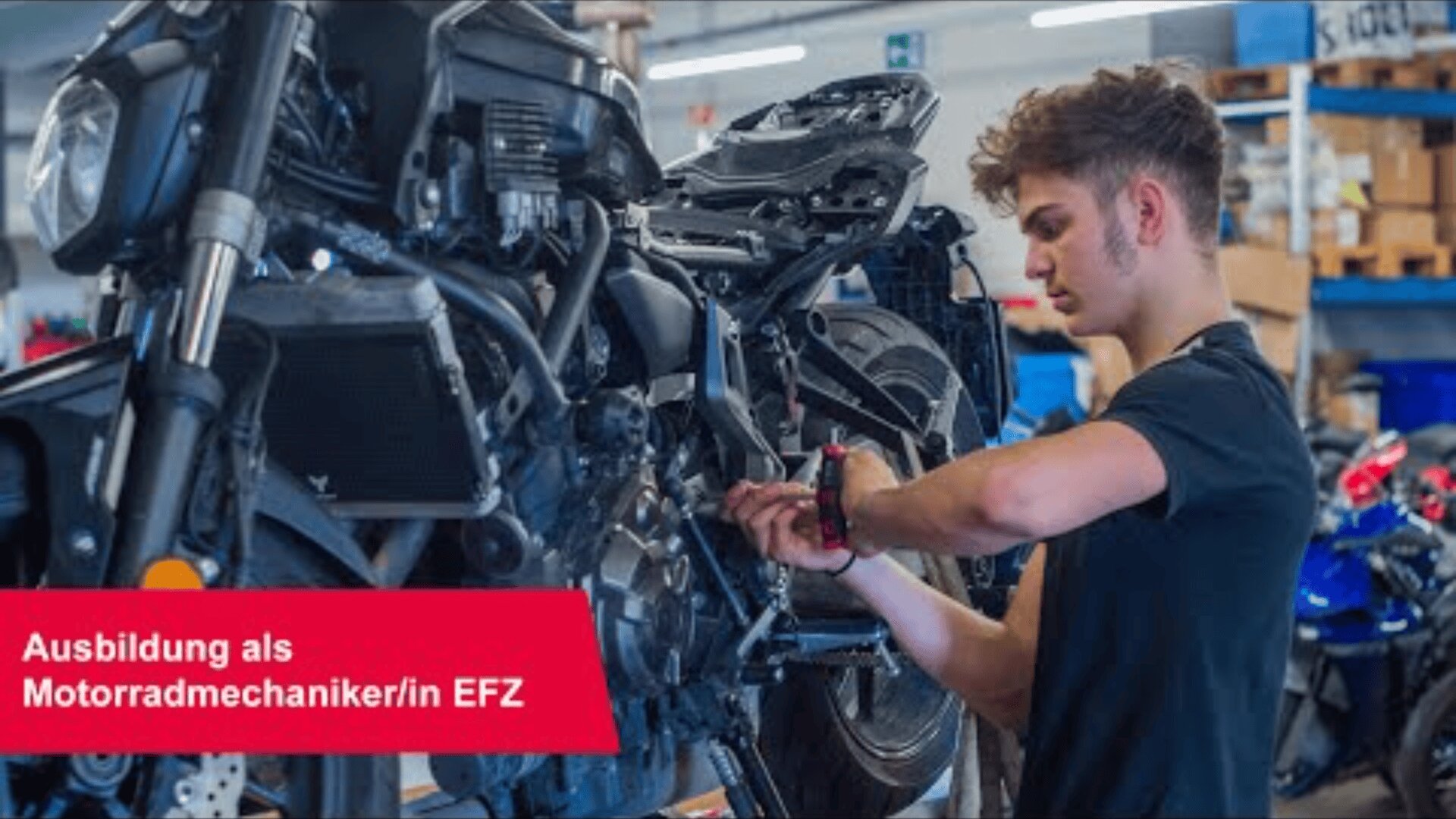 Ein junger Mann repariert ein Motorrad in einer Werkstatt, umgeben von Werkzeugen und Geräten. Unten links ist ein rotes Transparent mit der Aufschrift Ausbildung als Motorradmechaniker/in EFZ zu sehen.