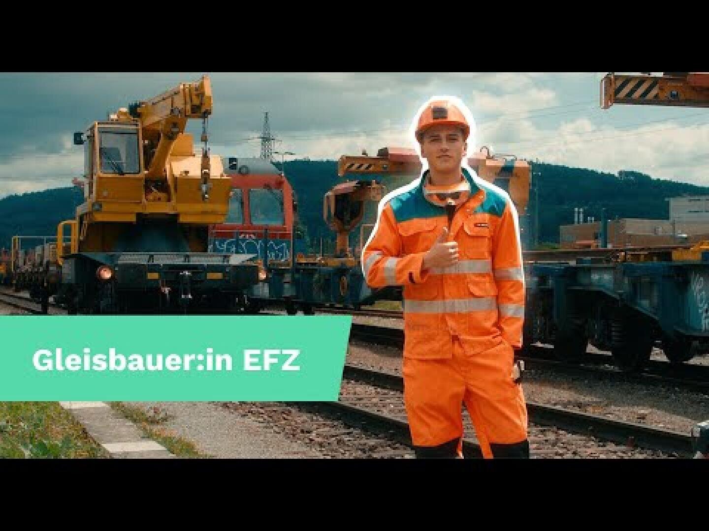 Eine Person in orangefarbener Schutzkleidung und Schutzhelm steht auf einem Bahngleis und zeigt den Daumen nach oben. Dahinter sind Eisenbahnwaggons und ein gelber Baukran zu sehen. Der Text auf dem Bild lautet: Gleisbauer:in EFZ.