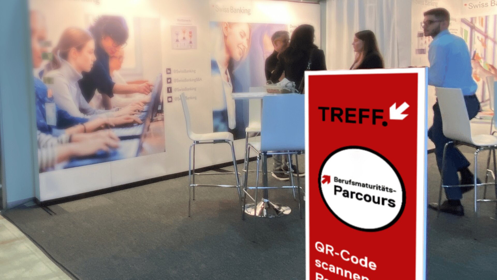 Eine Gruppe von Menschen steht und unterhält sich an Stehtischen an einem Stand einer Berufsmesse. Im Vordergrund steht ein rotes Schild mit der Aufschrift Berufsmaturitäts-Parcours und QR-Code scannen. Auf einem Wanddisplay hinter ihnen sind Laptop-Benutzer zu sehen.