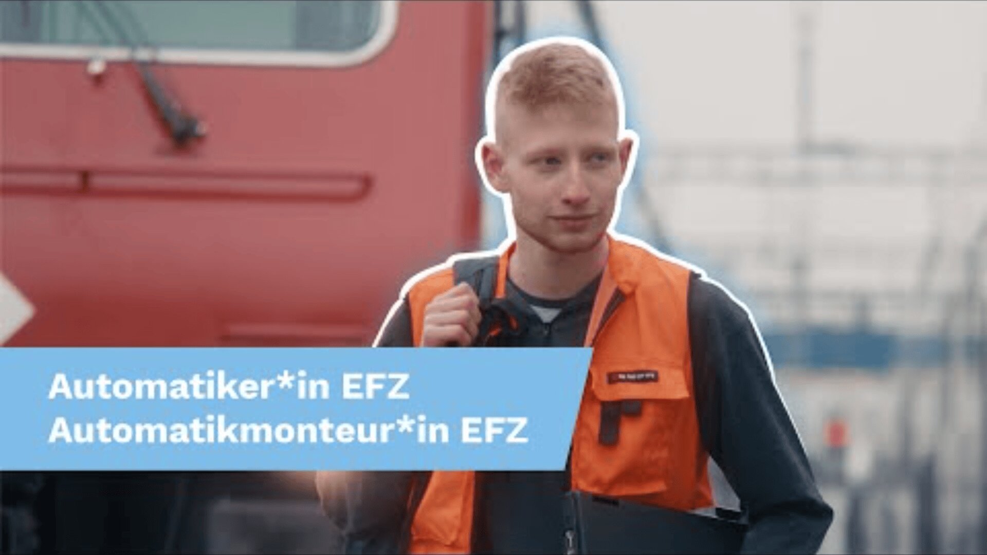 Eine Person mit kurzen roten Haaren, die eine orangefarbene Sicherheitsweste trägt, steht im Freien neben einem roten Zug. Auf einem blauen Transparent mit weisser Schrift steht: Automatiker*in EFZ Automatikmonteur*in EFZ.