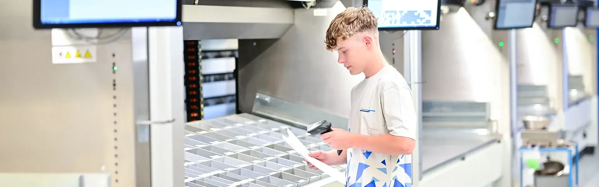 Ein junger Mann in einem Lagerhaus scannt in der Nähe einer automatisierten Sortieranlage ein Dokument mit einem Hand-Barcodescanner.