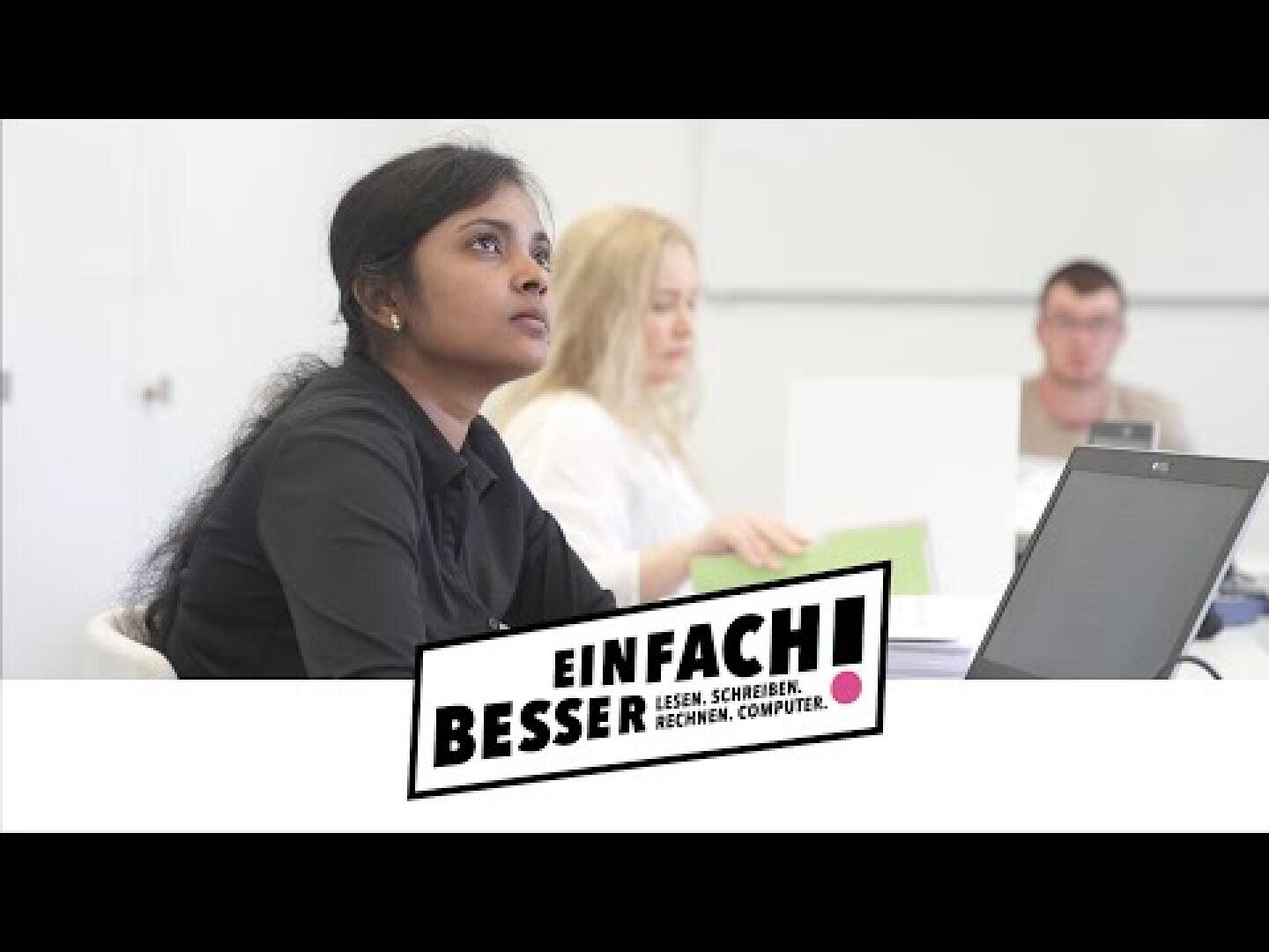 Eine Frau sitzt an einem Schreibtisch mit einem Laptop und schaut aufmerksam in ein Klassenzimmer. Im Hintergrund sind zwei weitere Personen zu sehen. Eine grafische Einblendung lautet Einfach besser! Lesen. Schreiben. Rechnen. Computer.