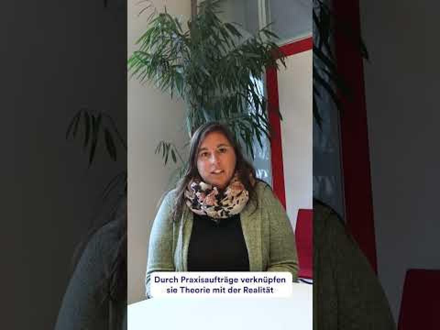 Eine Frau mit langen braunen Haaren, die eine grüne Strickjacke und einen geblümten Schal trägt, sitzt an einem Tisch in einem Innenraum. Hinter ihr befinden sich eine Pflanze, ein Fenster und rote Akzente. Der deutsche Text darunter lautet: Durch Praxisaufträge verknüpfen sie Theorie mit der Realität.