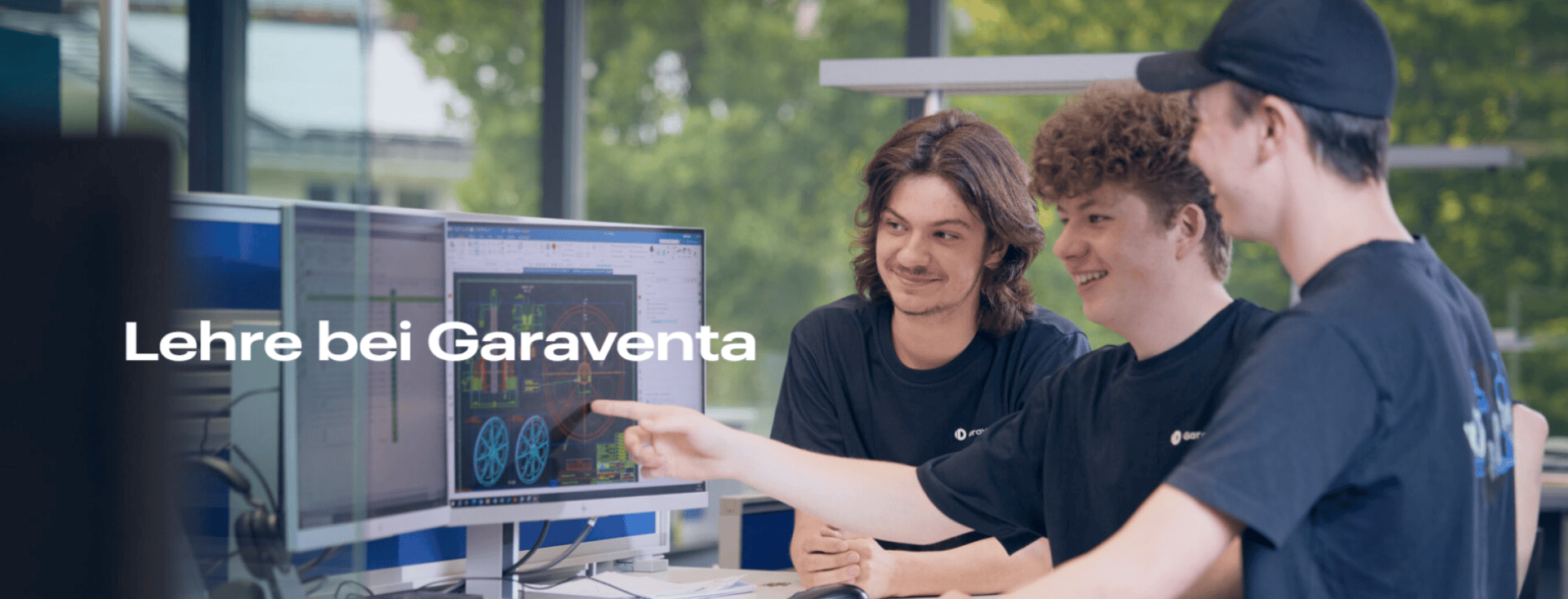 Drei junge Leute in schwarzen Hemden und Mützen lächeln, während sie gemeinsam an einem Computer arbeiten. Einer zeigt auf technische Diagramme auf einem Monitor. Der Text auf dem Bild lautet: "Lehre bei Garaventa". Draußen vor dem Fenster sind grüne Bäume zu sehen.