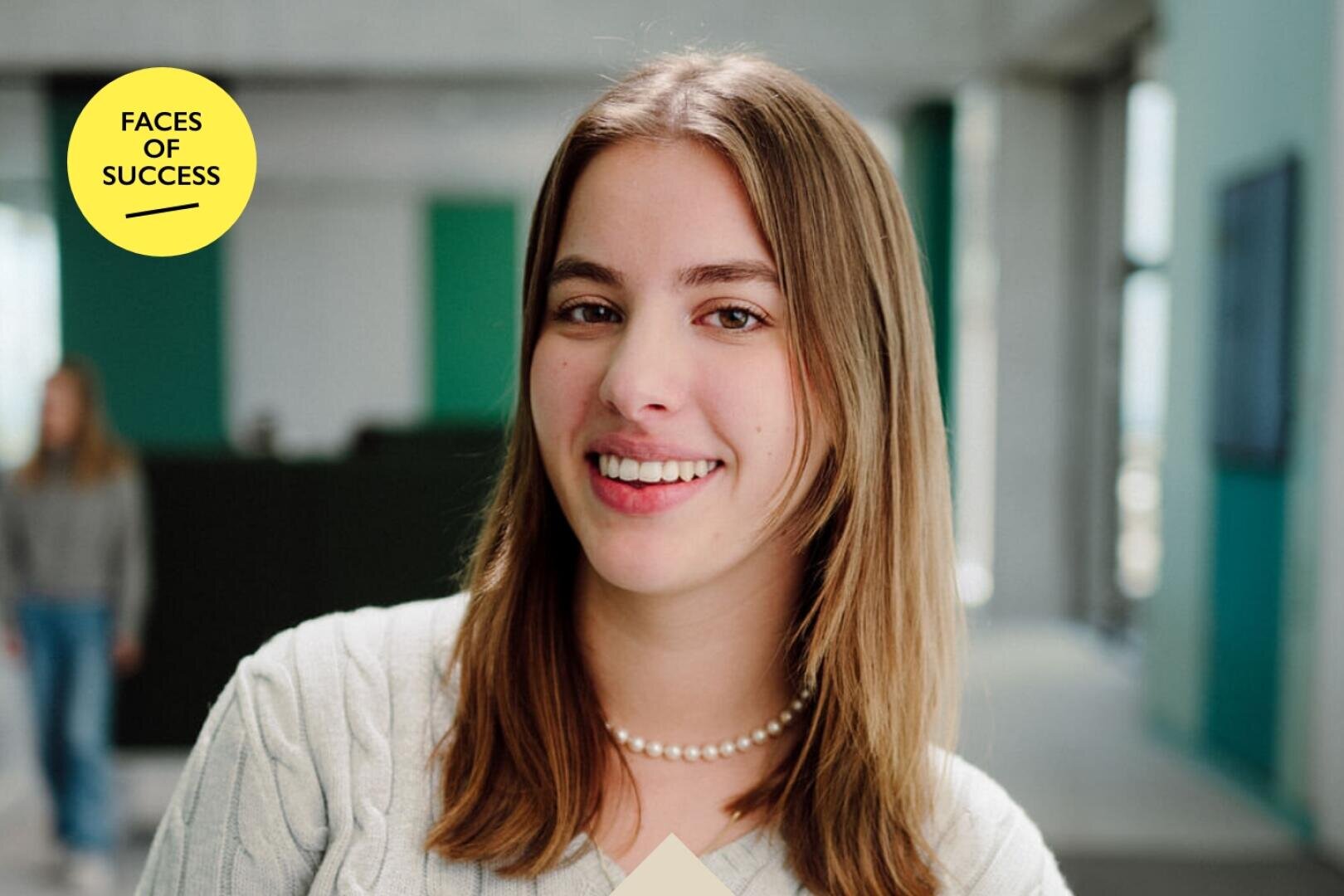 Eine junge Frau mit glattem braunem Haar, die einen hellen Pullover und eine Perlenkette trägt, lächelt in einer modernen Innenumgebung. In einem gelben Kreis auf dem Bild steht FACES OF SUCCESS.